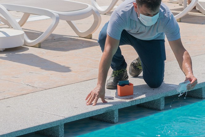 Man sieht einen Mann der Proben aus einem Schwimmbad nimmt.